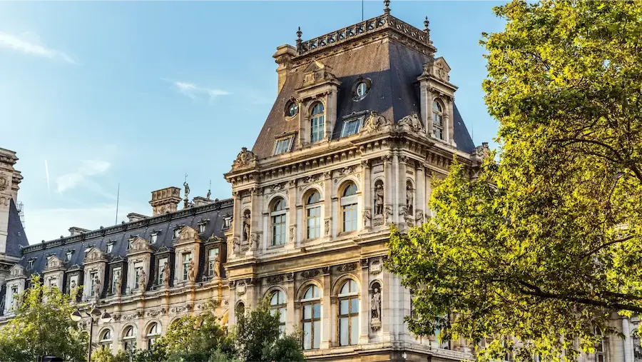 Façade ornée de l'Hôtel de Ville de Paris avec ses sculptures détaillées, ses fenêtres cintrées et ses toits à la Mansart sous une lumière dorée de fin de journée.